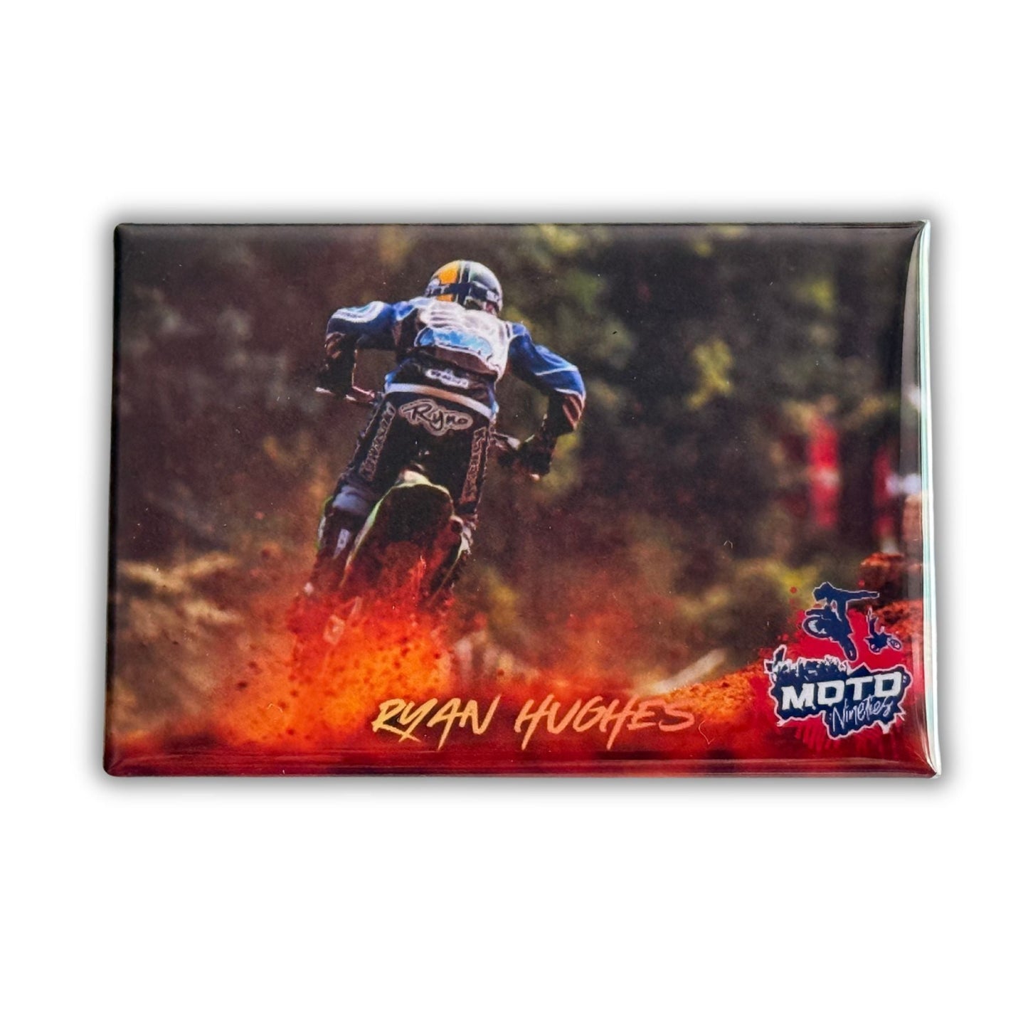 Ryan Hughes riding through a wooded motocross trail while throwing a large red dirt roost behind his motorcycle.
